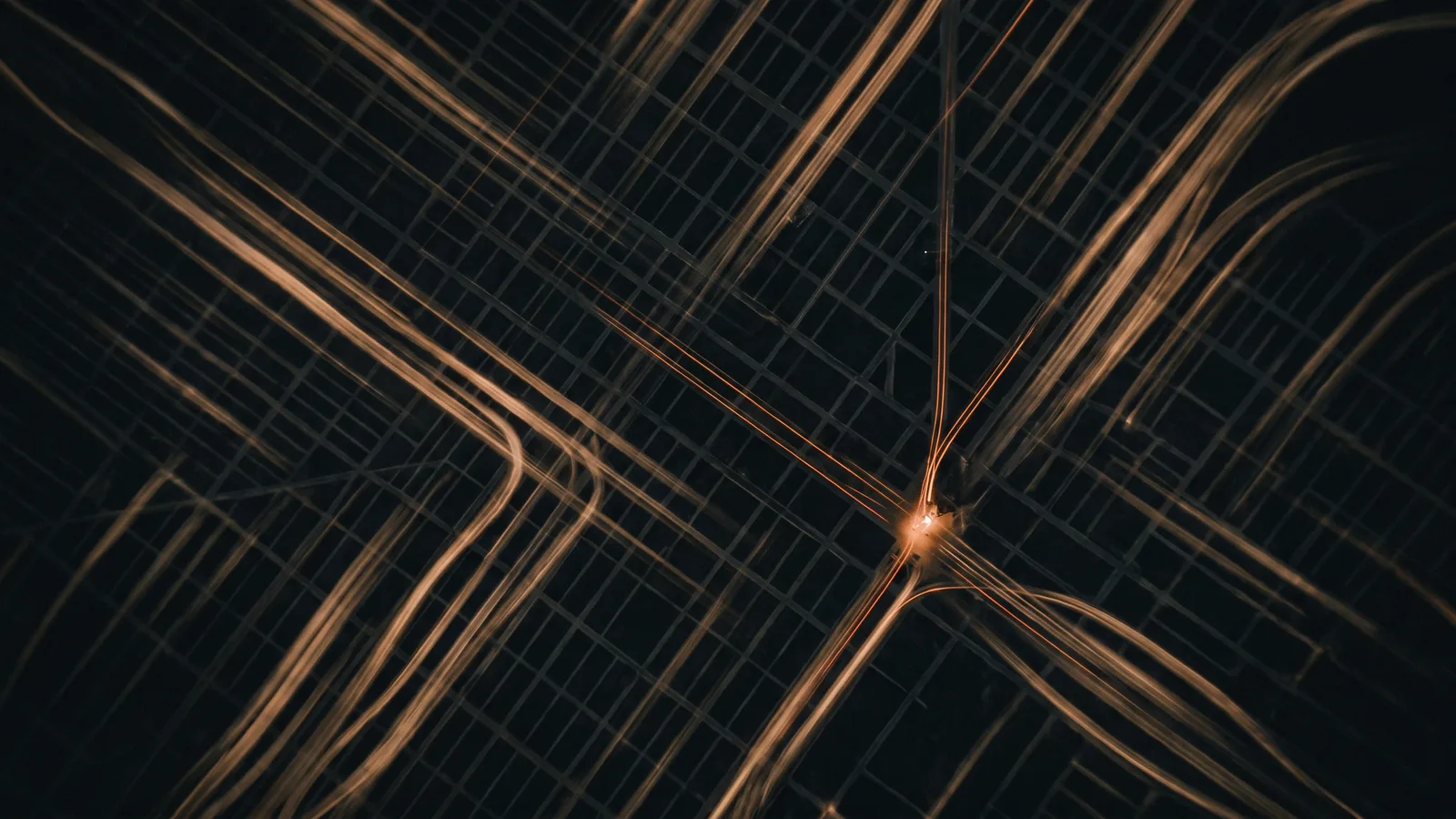 Aerial night photograph of amber light trails crossing a dark city grid, most of them veering away from a single bright point