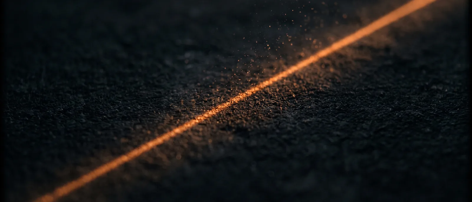 Macro photograph of a single thin line of orange light crossing a dark textured surface